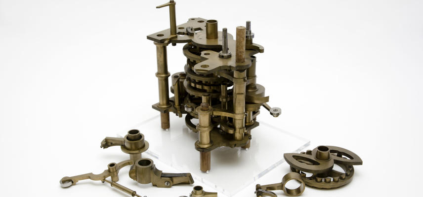 An image form the history of science showing pieces of the difference engine, an early computer, made of brass-coloured metal cogs and pieces