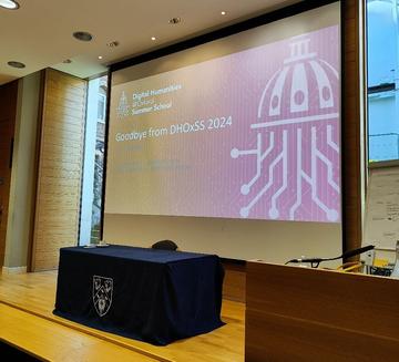 A table with blue tablecloth is in front of a slide showing the DHOXSS logo - the slide also contains the words "Goodbye from DHOXSS 2024" 