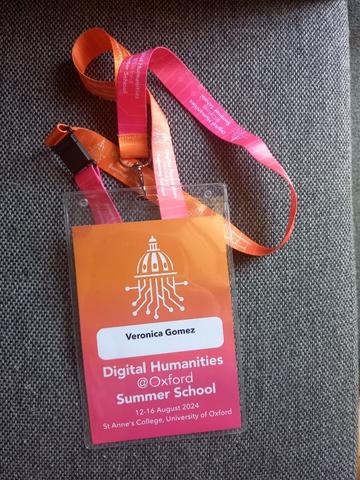 A bright orange and pink summer school lanyard with the DHOXSS logo and Veronica Gomez's name printed on it