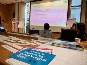 A lecture theatre with a slide showing text titled 'Primary key', in the foreground in a leaflet saying 'I want to improve group's digital skills'